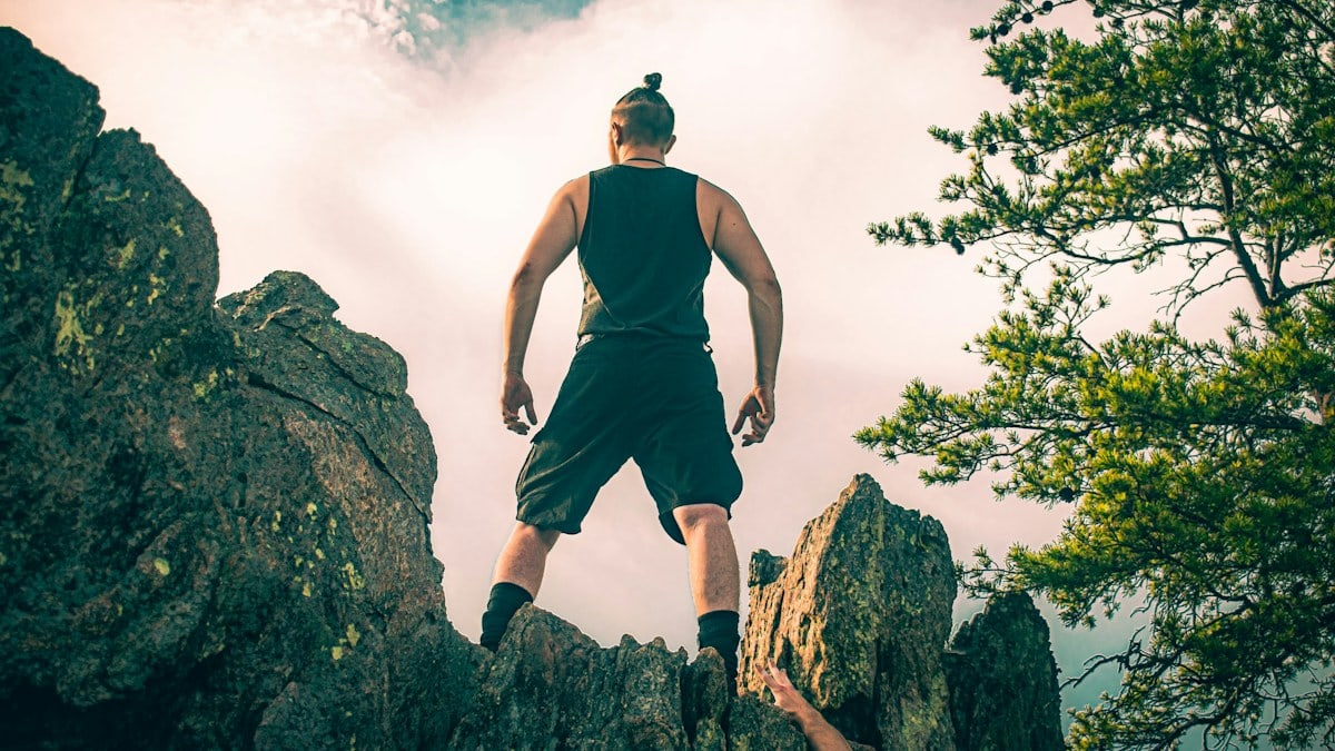 A man standing atop a mountain cliff edge staring into the sunset.